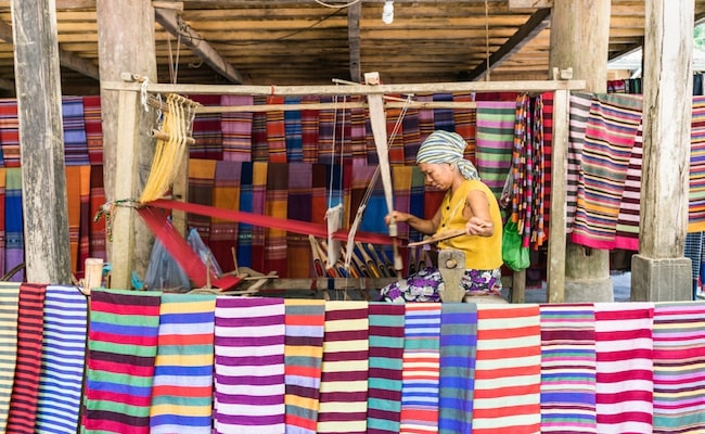 Local woman diligently working at a loom, weaving colourful brocade fabric